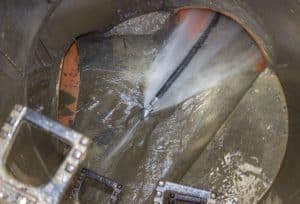 High-pressure water jet cleaning the interior of a large drain pipe, removing accumulated dirt and sludge from the pipe walls.